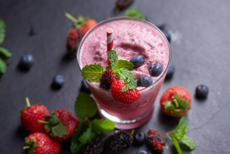 Creamy avocado smoothie in a glass with cacao nibs on top and fresh dates beside it