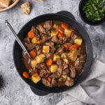 A slow cooker filled with hearty crockpot soup surrounded by fresh ingredients on a wooden table